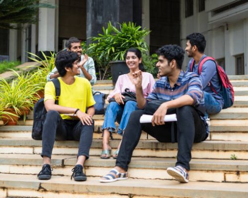 Group of happy students having chat with talking each other while sitting on college campus - concept of friendship, break time and communication.